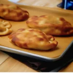 Freshly baked bolillo rolls on a wooden cutting board with assorted ingredients.